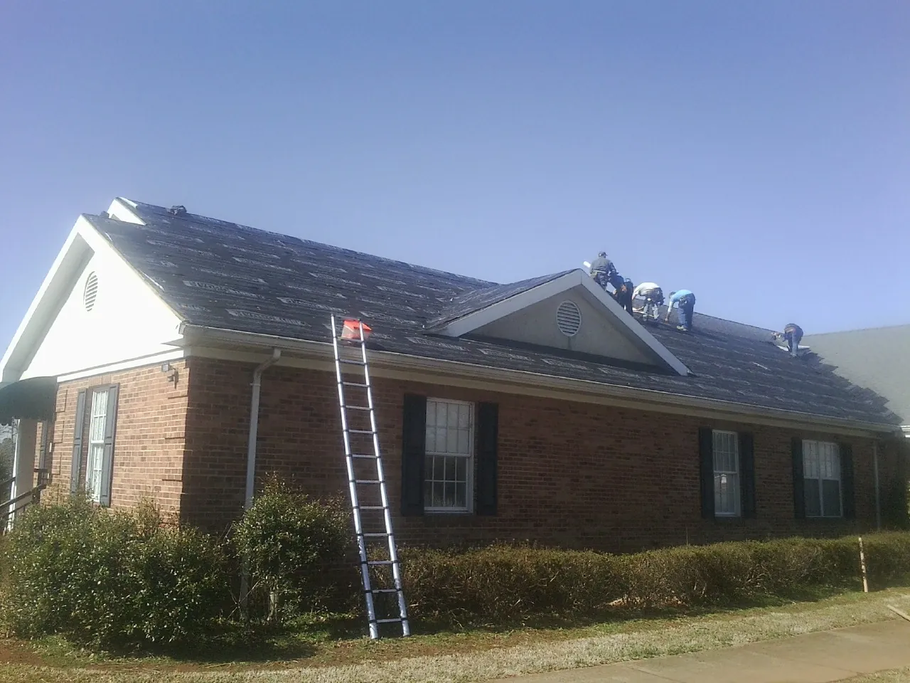 Crew tearing shingles off a brick ranch roof with a ladder set — Metal Roof Repair work by our crew in Turbeville