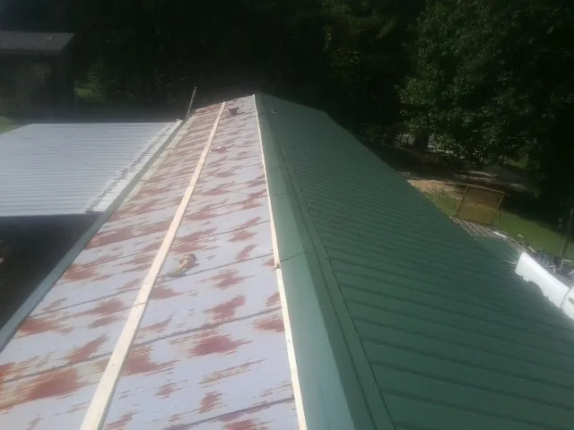 Old rusted panels beside newly installed green metal roofing — Wind Damage Roof Repair by Roofing Brothers in Turbeville