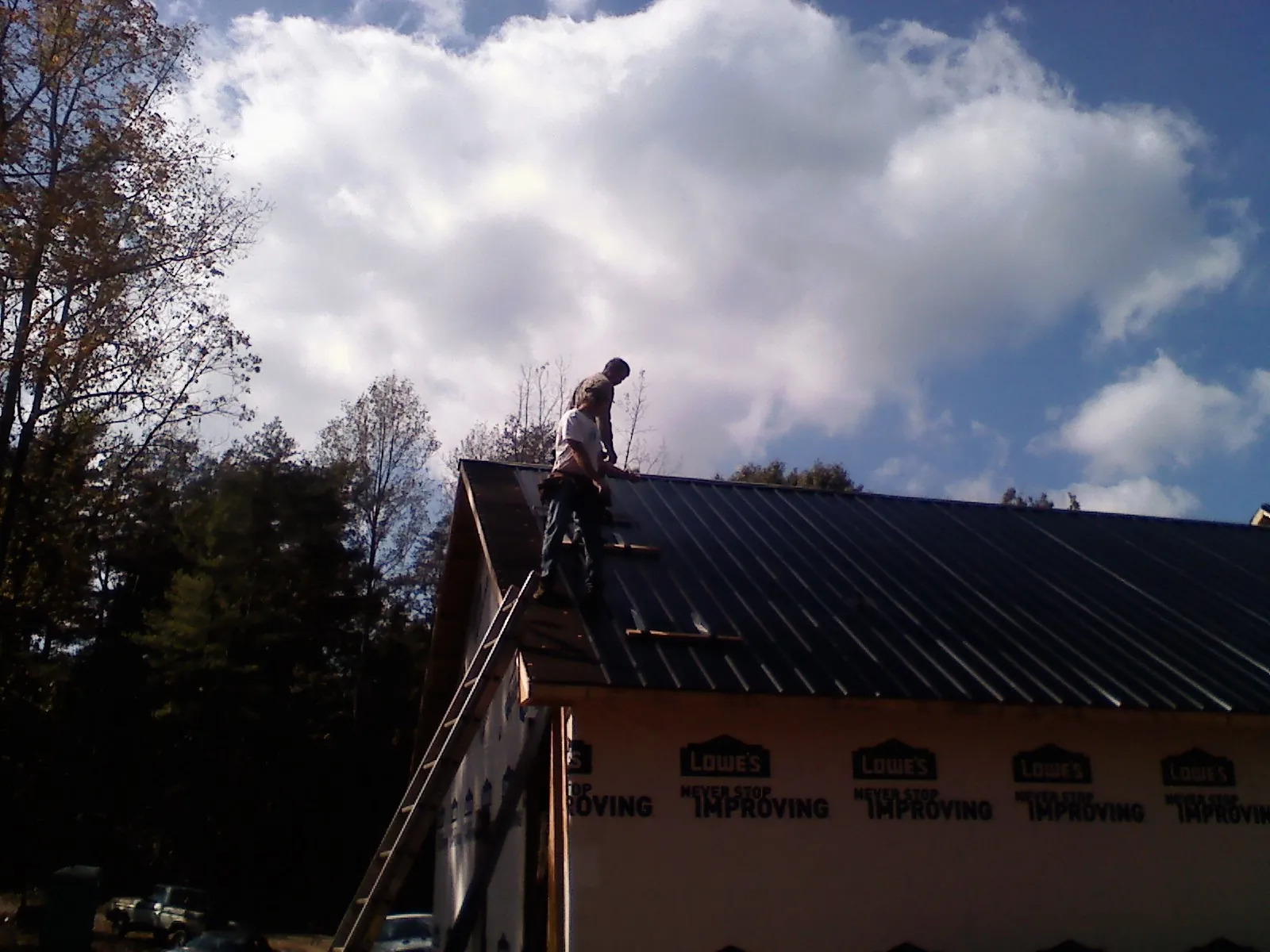 Roofer fastening dark metal panels high against a cloudy sky, from a Roof Inspection job in Turbeville