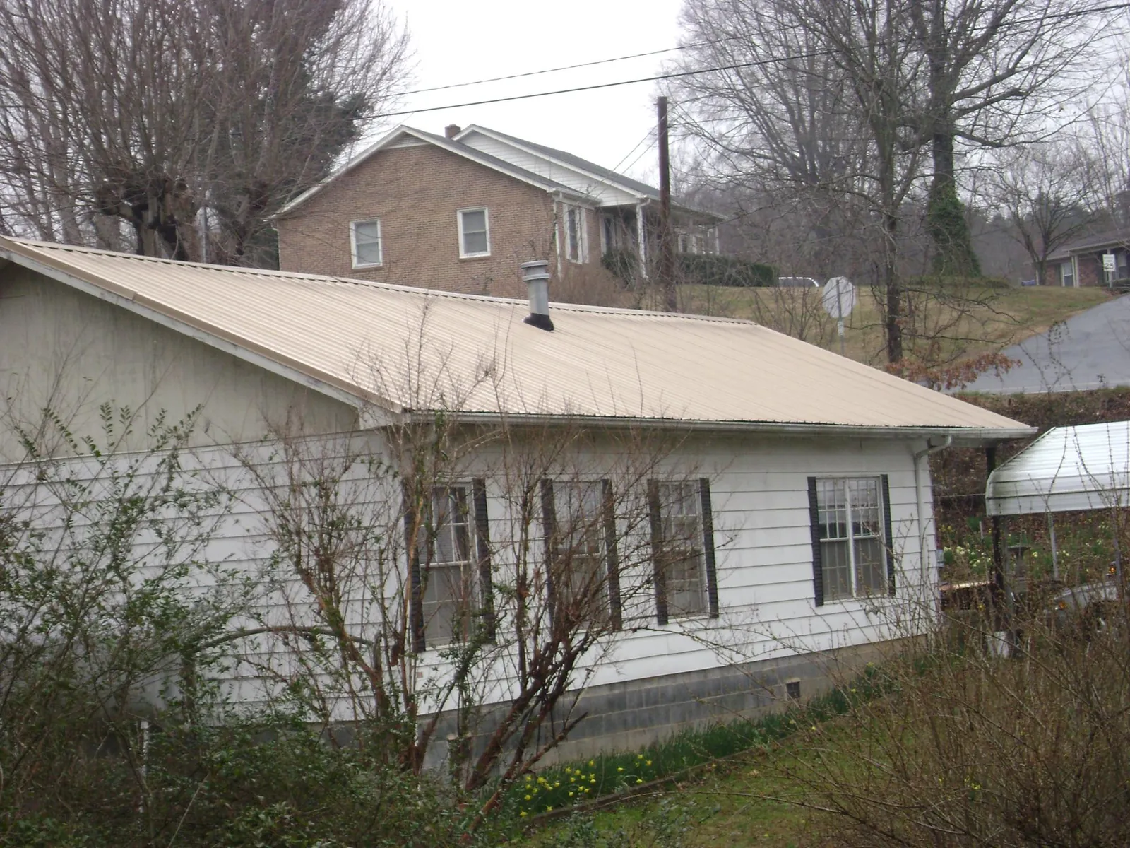 Tan metal roof on a white sided house set into a hillside — Commercial Roofing by Roofing Brothers in Turbeville